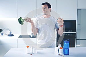 Young doctor skeptically looking at the broccoli and choosing a pill