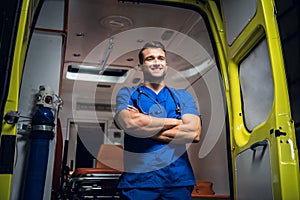 Young doctor standing and smiling in front of an an ambulance car