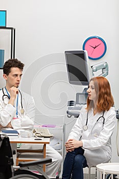 A young doctor talks to a redheaded intern about his next patient. GP. Doctor's office