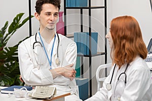 A young doctor talks to a redheaded intern about his next patient. GP. Doctor's office