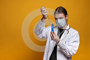 Young doctor using a pipette and a blue tube, wearing protection mask and a stethoscope is trying to find a vaccine