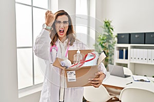 Young doctor woman holding box with medical items annoyed and frustrated shouting with anger, yelling crazy with anger and hand