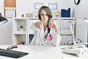 Young doctor woman holding electronic cigarette at medical clinic pointing with finger to the camera and to you, confident gesture