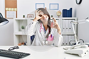 Young doctor woman holding electronic cigarette at medical clinic smiling happy doing ok sign with hand on eye looking through