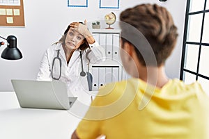 Young doctor woman with patient at the clinic stressed and frustrated with hand on head, surprised and angry face