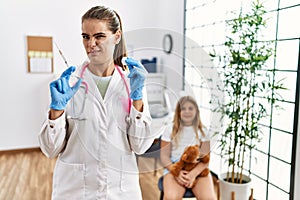 Young doctor woman putting vaccine to little girl clueless and confused expression