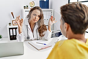 Young doctor woman showing electronic cigarette and normal cigarrete to patient skeptic and nervous, frowning upset because of
