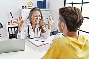 Young doctor woman showing electronic cigarette and normal cigarrete to patient smiling and laughing hard out loud because funny