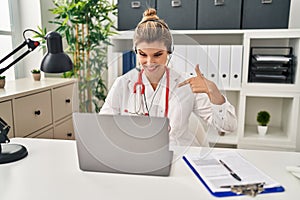 Young doctor woman wearing doctor uniform working using computer laptop pointing finger to one self smiling happy and proud