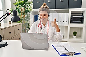 Young doctor woman wearing doctor uniform working using computer laptop smiling happy and positive, thumb up doing excellent and