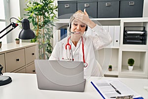 Young doctor woman wearing doctor uniform working using computer laptop stressed and frustrated with hand on head, surprised and