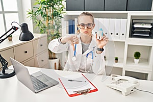 Young doctor woman wearing uniform and stethoscope with angry face, negative sign showing dislike with thumbs down, rejection