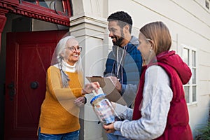 Young door to door fundraisers talking to senior woman and collecting money for charity in street.