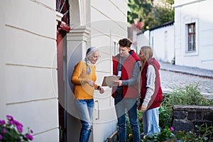 Young door to door volunteers talking to senior woman and taking survey at her front door.