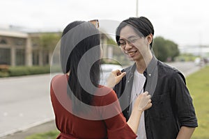 A young doting asian woman fixes her boyfriend\'s jacket. A loving girlfriend showing care and affection to her partner