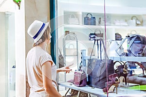 Young doubting girl looking at shop window with shoes and bags in Shopping Mall. Shopper. Sales. Shopping Center. Space for text.