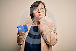 Young down syndrome business woman holding credit card as customer payment serious face thinking about question, very confused