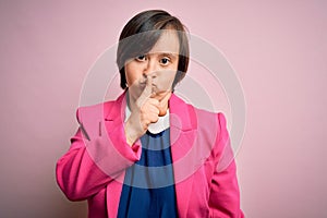 Young down syndrome business woman over pink background asking to be quiet with finger on lips