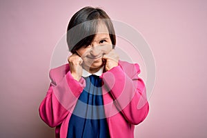 Young down syndrome business woman over pink background covering ears with fingers with annoyed expression for the noise of loud