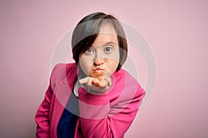 Young down syndrome business woman over pink background looking at the camera blowing a kiss with hand on air being lovely and