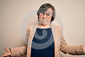 Young down syndrome business woman wearing glasses standing over isolated background clueless and confused expression with arms