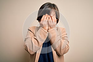 Young down syndrome business woman wearing glasses standing over isolated background with sad expression covering face with hands