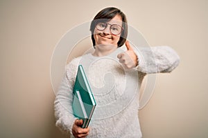 Young down syndrome student woman reading a book from library over isolated background happy with big smile doing ok sign, thumb