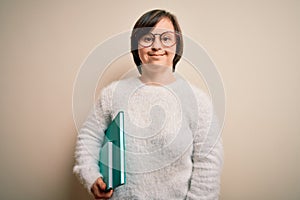 Young down syndrome student woman reading a book from library over isolated background with a happy face standing and smiling with