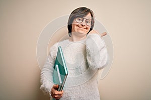 Young down syndrome student woman reading a book from library over isolated background very happy pointing with hand and finger to