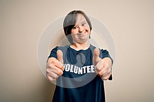 Young down syndrome volunteer woman wearing social care charity t-shirt approving doing positive gesture with hand, thumbs up
