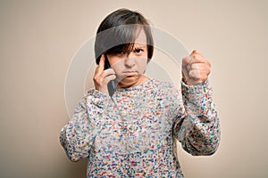 Young down syndrome woman having a conversation speaking on smartphone annoyed and frustrated shouting with anger, crazy and