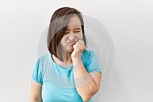 Young down syndrome woman standing over isolated background looking stressed and nervous with hands on mouth biting nails