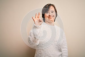 Young down syndrome woman standing over isolated background showing and pointing up with fingers number three while smiling