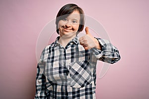 Young down syndrome woman wearing casual shirt over pink background doing happy thumbs up gesture with hand