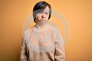 Young down syndrome woman wearing casual sweater over yellow background skeptic and nervous, frowning upset because of problem