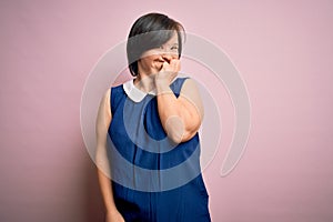 Young down syndrome woman wearing elegant shirt over pink background looking stressed and nervous with hands on mouth biting nails