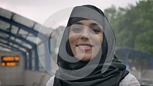 Young dreaming muslim woman in hijab is smiling on railway station, religion concept, urban concept