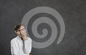 Young dreamy male thinker pensively looks at free space for text on gray background.