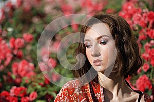 Young dreamy woman with red roses. Outdoor portrait of a romantic girl with hard sunlight. Space for text