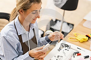 Young dressmaker woman sews clothes on working table. Smiling seamstress and her hand close up in workshop. Focus on suture on