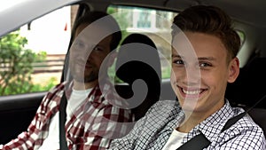 Young driver and his father smiling into camera, teen getting driving license