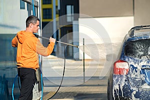 Young driver man washing his car with contactless high pressure water jet in self service car wash