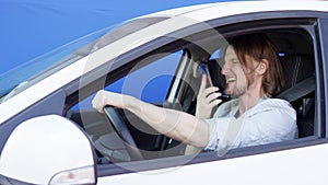 Young driver is quarrelling on the cellphone. Annoyed man is shouting and beating his phone on the passenger seat