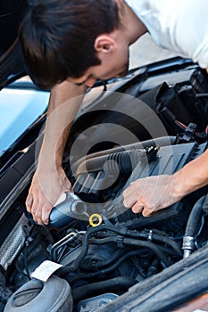 Young driver replace motor oil in car on street