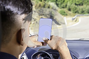 Young driver, using smartphone, on the road in the car