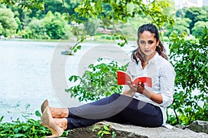 Young East Indian American Woman reading red book, relaxing at Central Park, New York