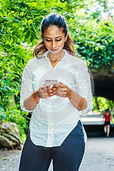 Young East Indian American Woman texting on cell phone outdoor at Central Park, New York