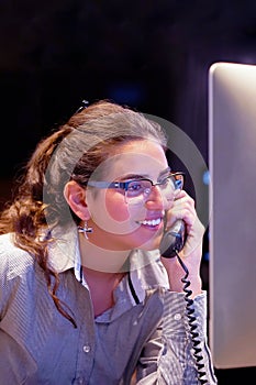 Young efficient secretary working in the office, she is answering phone calls. Customer service concept. Night time