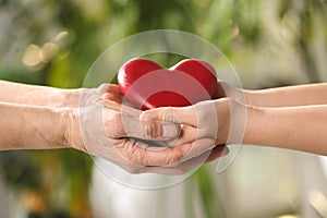 Young and elderly women holding red heart in hands on blurred green background, closeup