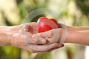 Young and elderly women holding red heart in hands on blurred green background, closeup